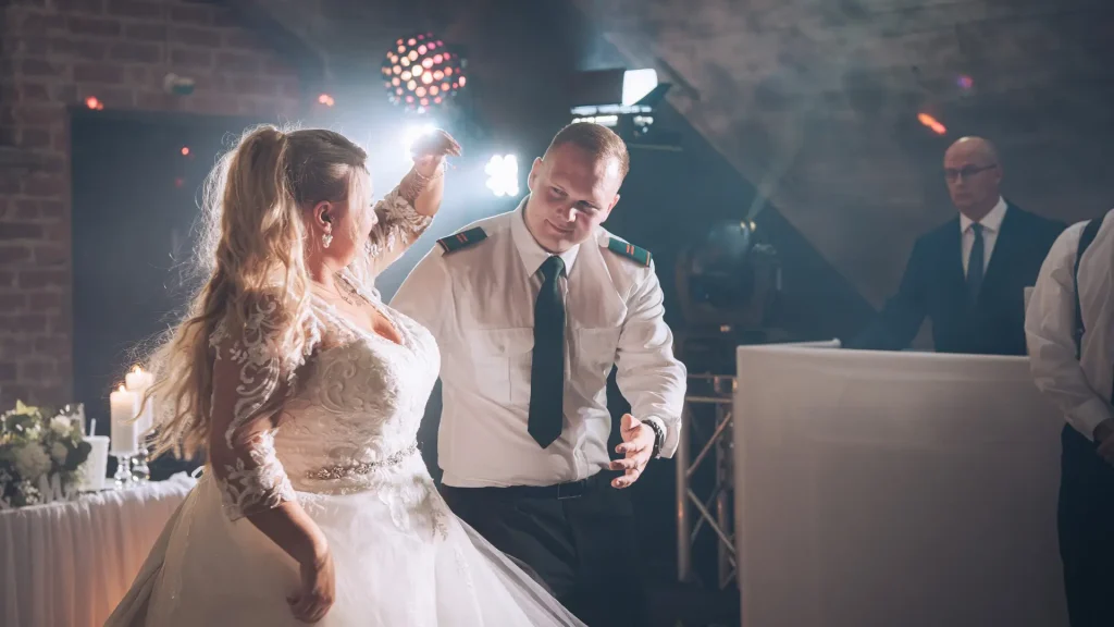 Tanssiva hääpari, taustalla dj, rustiikkinen milljöö, juhlavalaistus
